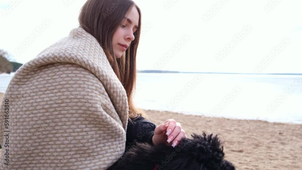 A beautiful girl in a plaid relaxes on the seashore with her pet and drinks tea A beautiful girl in a plaid relaxes on the seashore with her pet and drinks tea