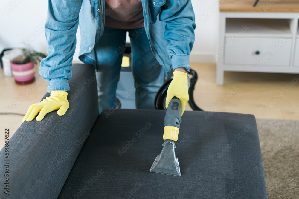 Cleaning service company employee removing dirt from furniture in flat with professional equipment. Man arm cleaning sofa with washing vacuum cleaner close up