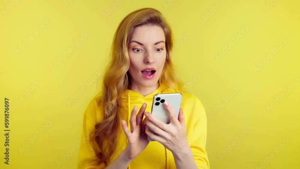 Surprised young woman pointing at mobile phone. Wow! Lady amazed excited with smartphone for social media, online streaming, news and internet, surprise face. Studio shot isolated on yellow background Surprised young woman pointing at mobile phone. Wow! Lady amazed excited with smartphone for social media, online streaming, news and internet, surprise face. Studio shot isolated on yellow background