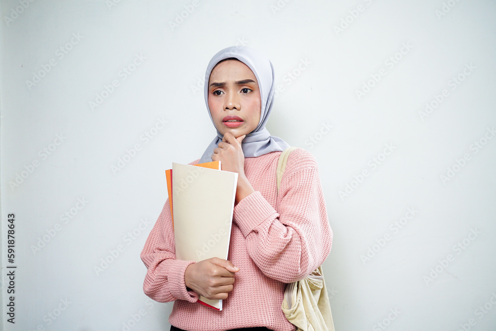 Smiling Asian Muslim female student in pink sweater with medium bag, holding book and thinking isolated on white background. back to school concept Smiling Asian Muslim female student in pink sweater with medium bag, holding book and thinking isolated on white background. back to school concept
