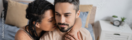 young african american woman with dreadlocks hugging bearded boyfriend in bedroom at home, banner.