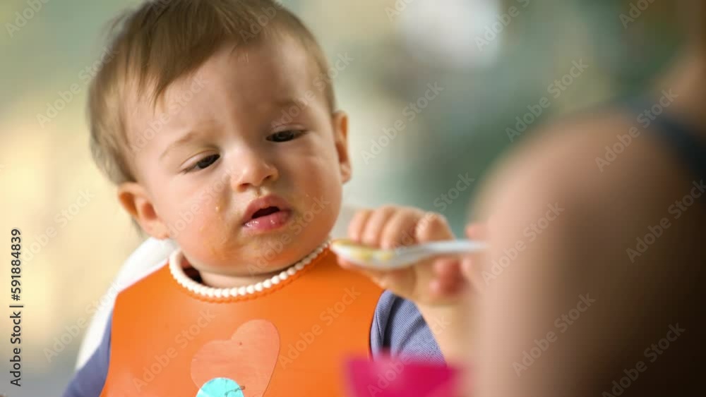 Mother feeding her baby son with fruit vegetable puree in baby chair. The baby crying and does not want to eat Mother feeding her baby son with fruit vegetable puree in baby chair. The baby crying and does not want to eat
