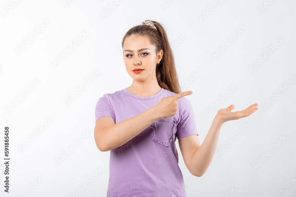 Young woman with long hair pointing finger right with disappointing look, stands in casual t shirt over white background Young woman with long hair pointing finger right with disappointing look, stands in casual t shirt over white background