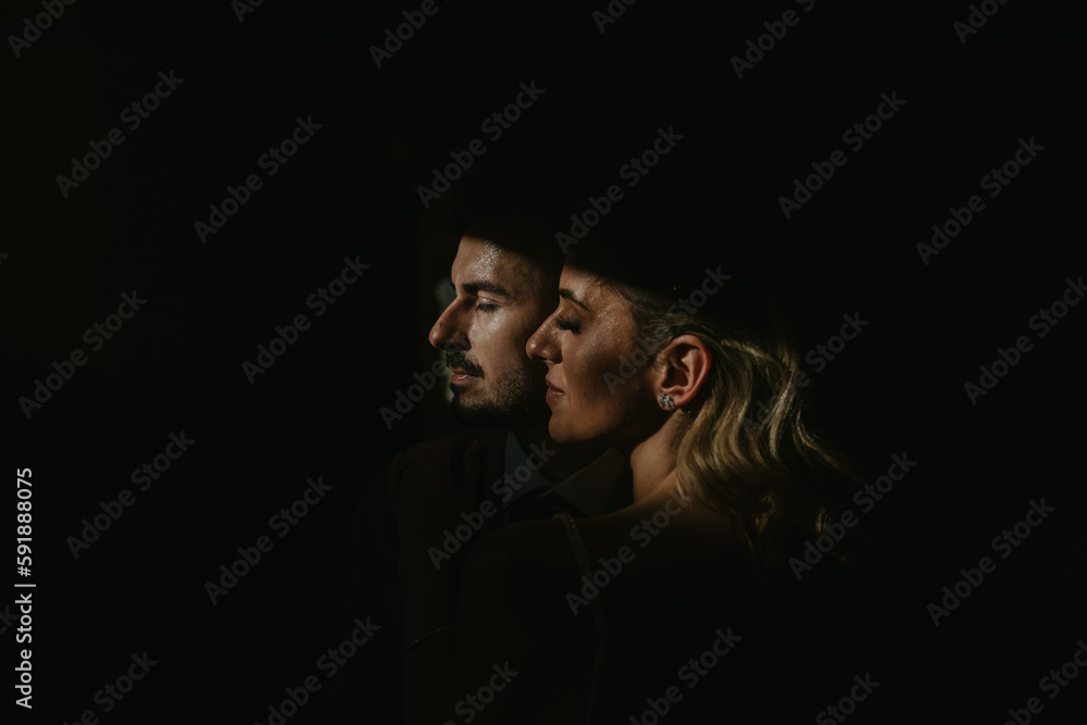 © Amar Socic2/Wirestock Creators - Profiles of a Caucasian male and a Middle Eastern female in the darkness on black background