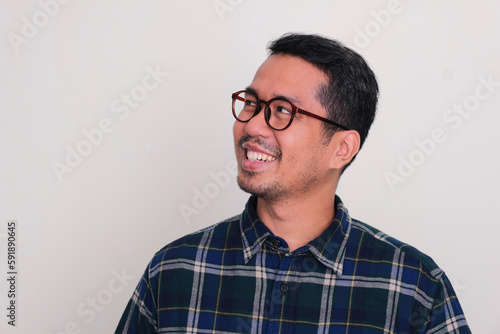 Close up shot of adult Asian man wearing glasses smiling and looking to the right side © KrishnaTedjo