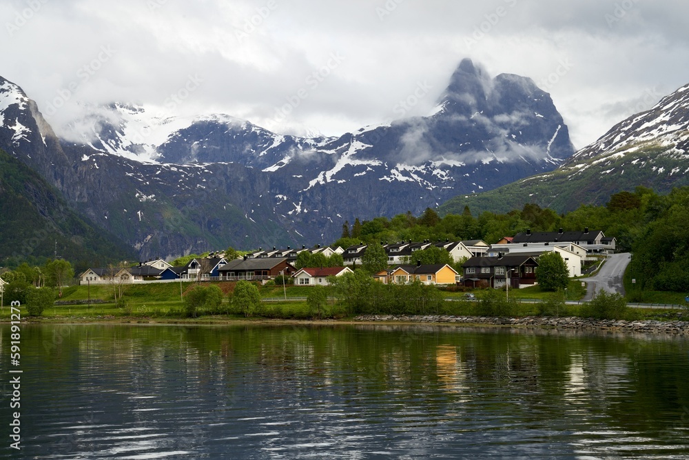 Wooden residential houses near snow-covered mountain peaks and a lake, Fjord coast, Norway
