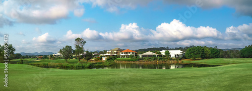 Wide panoramic view of premium lush golf course with beautiful pond in the foreground, surrounded by green grass and trees. 