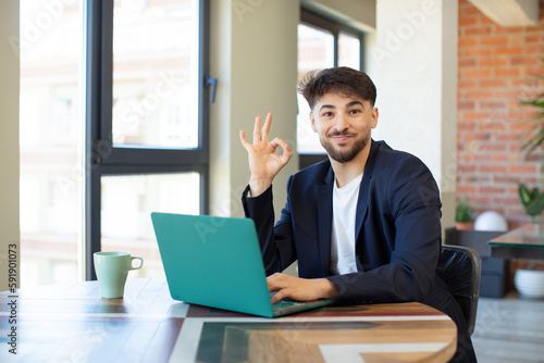 young handsome man feeling happy, showing approval with okay gesture. freelance concept with laptop