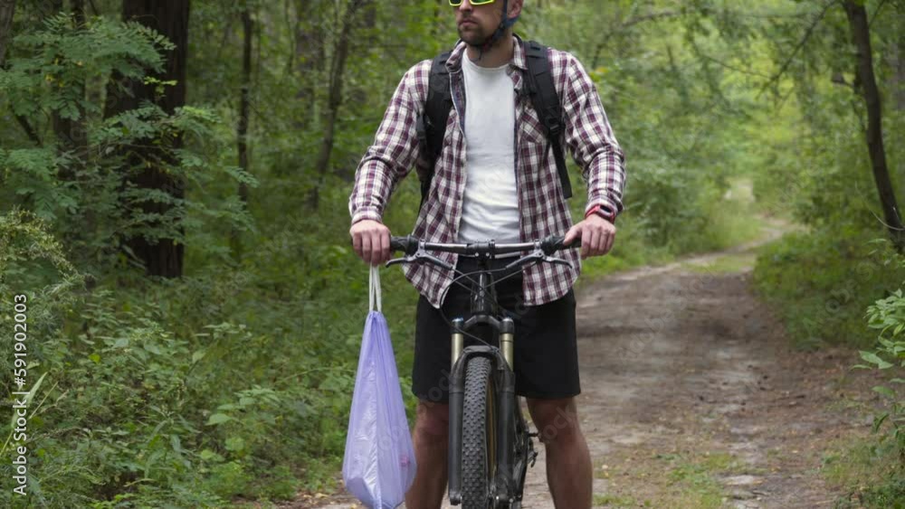 Portrait of male cyclist picking up trash in woods on bicycle ride