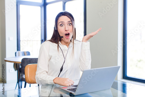 young pretty woman looking surprised and shocked, with jaw dropped holding an object. telemarketer concept