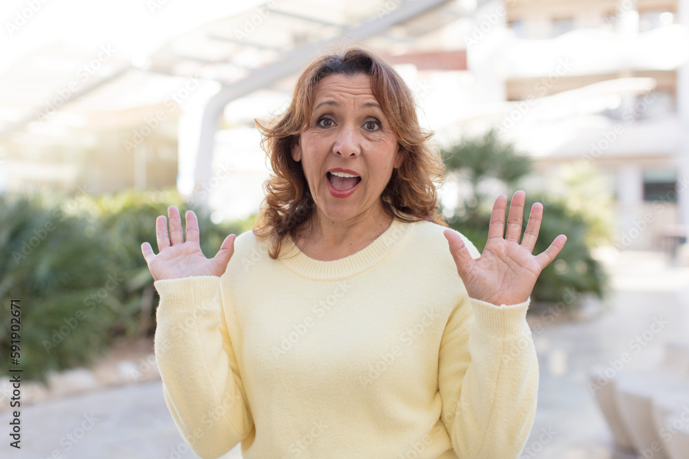 middle age woman looking happy and excited, shocked with an unexpected surprise with both hands open next to face