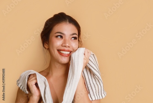 Portrait of beautiful Asian a woman with natural makeup holding white face towel standing over beige background, copy space.