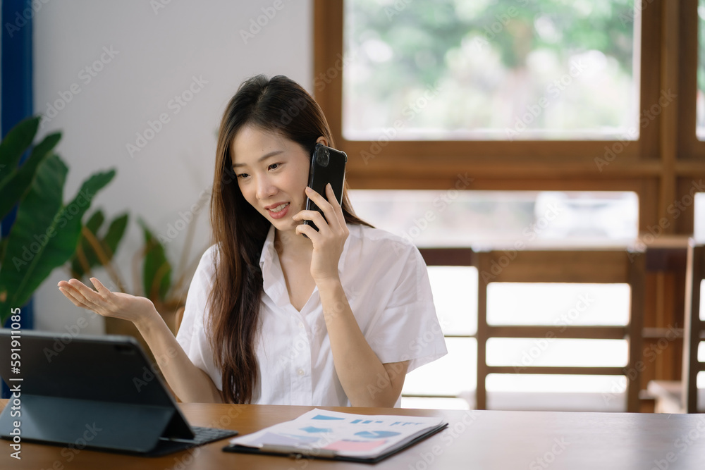 Asian woman talking mobile phone and working on laptop and on table at home office. Asian woman talking mobile phone and working on laptop and on table at home office.