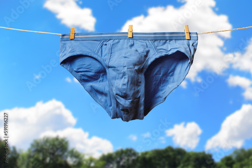Clean blue men's briefs hanging on rope to dry outdoors on sunny summer day. Clothesline with washed underwear. Regular laundry. Hygiene and clothes care concept.