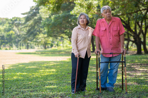 An old elderly Asian man uses a walker and walks in the park with his wife. Concept of happy retirement With Love and care from family and caregiver, Savings, and senior health insurance