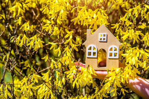 The girl holds the house symbol against the background of blossoming forsythia