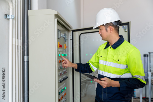 An engineer or electrician working push button on electrical system of water supply system controller with tablet at factory.