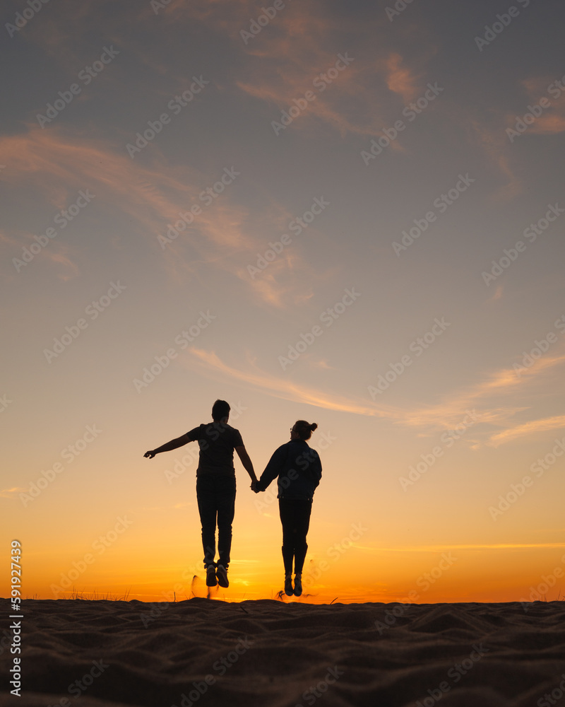 couple of man and woman holding hands jumping on background of the sky. sunset walk on seashore, nature background. joke and fun, relationships and carefree communication