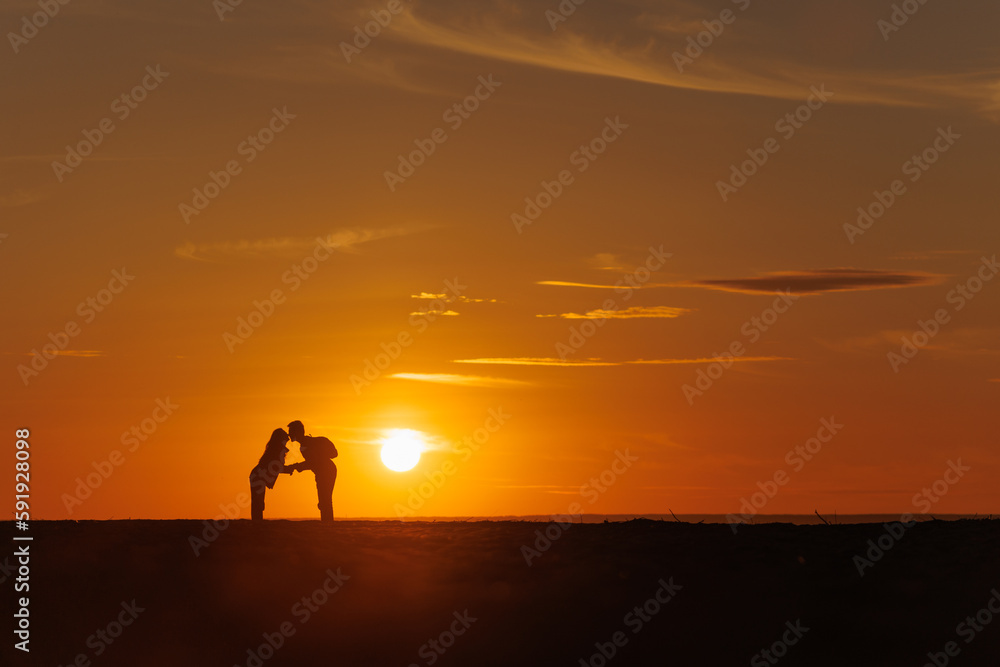 silhouette of couple at sunset, woman and man holding hands walking along seashore in rays of sunset sunlight. walk and hug. place for text, romantic relationships, freedom and carelessness