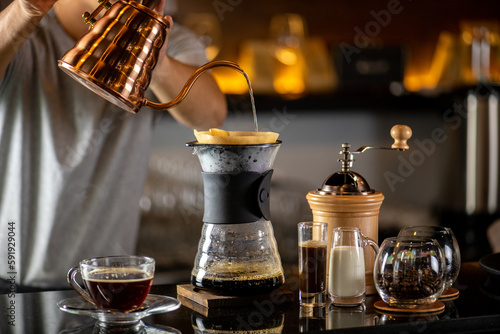 drip coffee  Barista making drip coffee by pouring spills hot water on coffee ground with prepare filter from copper pot to glass transparent chrome drip maker on wooden table in cafe shop