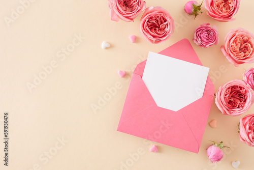 Flat lay photo of open envelope with white card natural flowers pink rose buds and small hearts on isolated light beige background with empty space. Mother's Day love concept