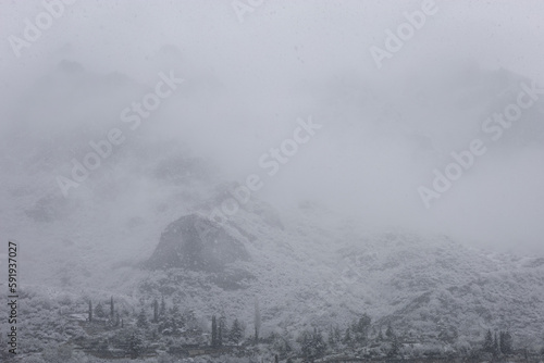 Steep rocky mountain chain covered with fresh snow and covered by fog during a snowstorm