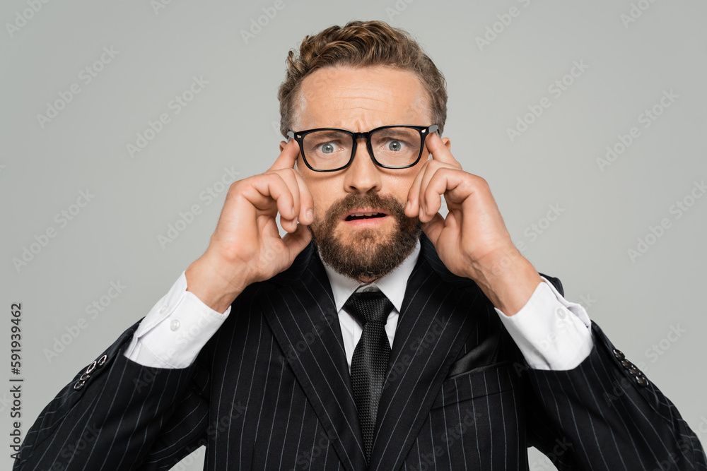 stressed businessman in formal wear and glasses looking at camera isolated on grey.