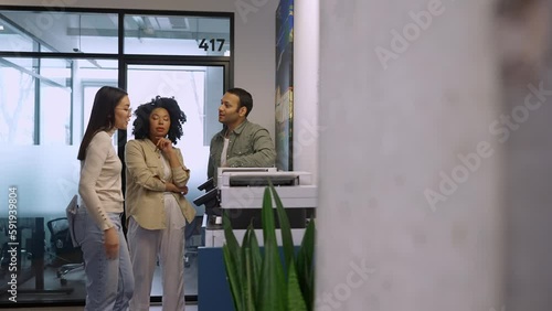 Serious multinational colleagues print documents on printer and talk in office