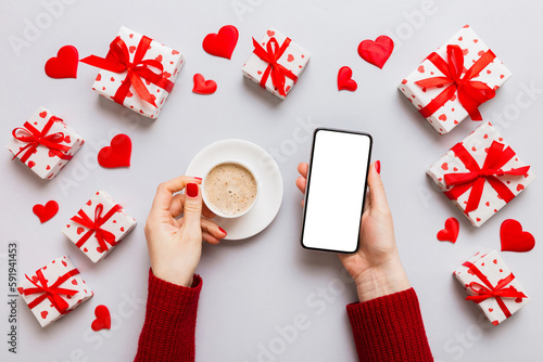 Female hands holding smart phone with coffee for Valentine day, gift box and envelope, hearts