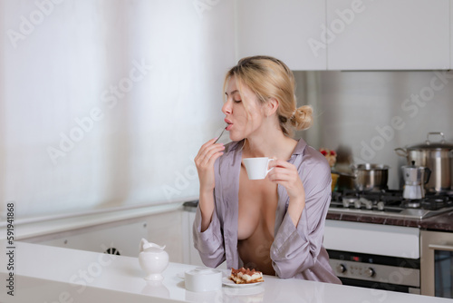 Sexy woman drink coffee in the kitchen. Woman wearing sexy pajama with bare breast relaxing in home kitchen. Young sexy housewife in seductive underwear prepare coffee in the kitchen. photo
