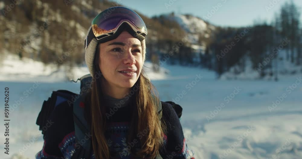 Portrait of Female Tourist with Backpack and Ski Goggles Enjoying the Beautiful Scenery in Snowy Mountain. Active Smiling Woman Looking at Camera and Posing in Winter. Slow Motion Portrait of Female Tourist with Backpack and Ski Goggles Enjoying the Beautiful Scenery in Snowy Mountain. Active Smiling Woman Looking at Camera and Posing in Winter. Slow Motion