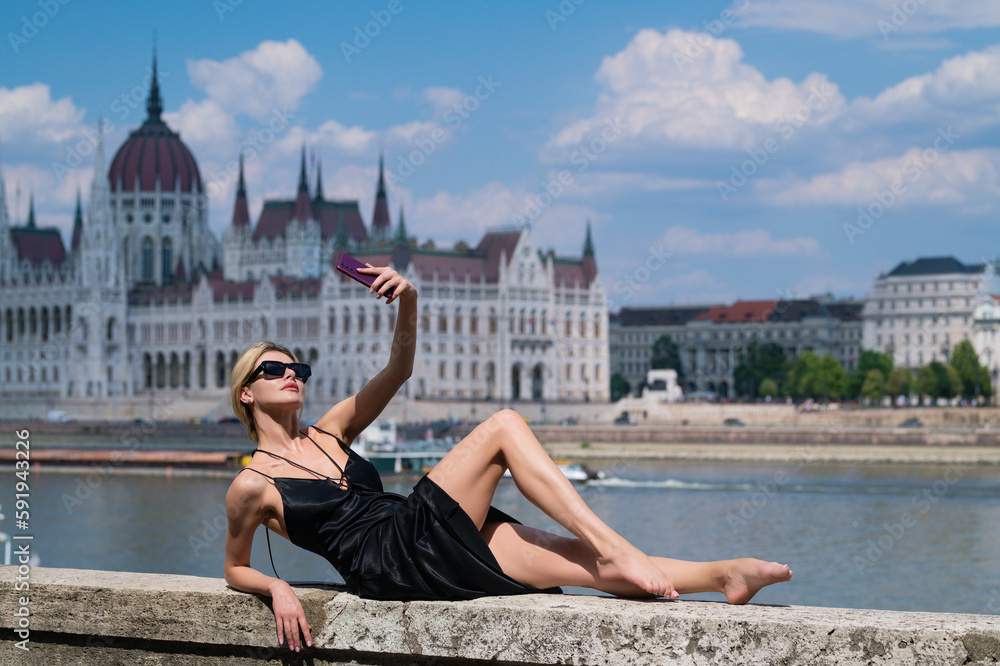 Fototapeta premium Fashion woman. Sexy trendy girl posing at the city in Europe. Summer street fashion. Luxury woman posing near Budapest Parliament in Hungary. High Fashion model girl posing outdoor. Fashion dress.