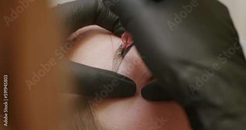 The master makes permanent eyebrow makeup with a needle tattoo machine. permanent makeup tattoo close up. Microblading brows tattooing. Dark pigment is injected under skin. Cosmetology procedure. photo