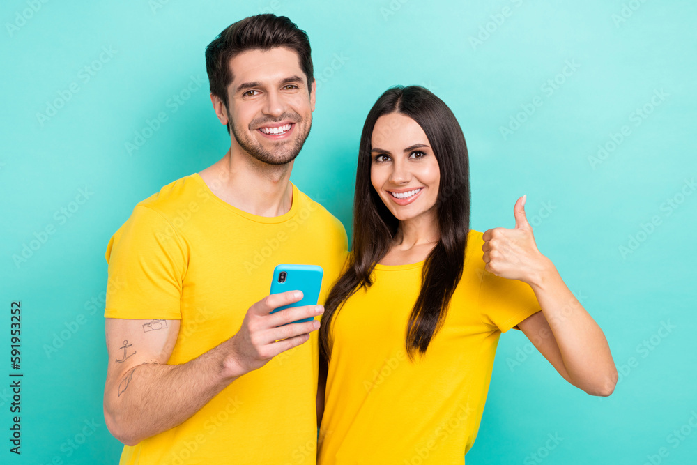 Photo of cheerful new smartphone users young two people friends thumb up recommend modern technology check email isolated on cyan color background Photo of cheerful new smartphone users young two people friends thumb up recommend modern technology check email isolated on cyan color background
