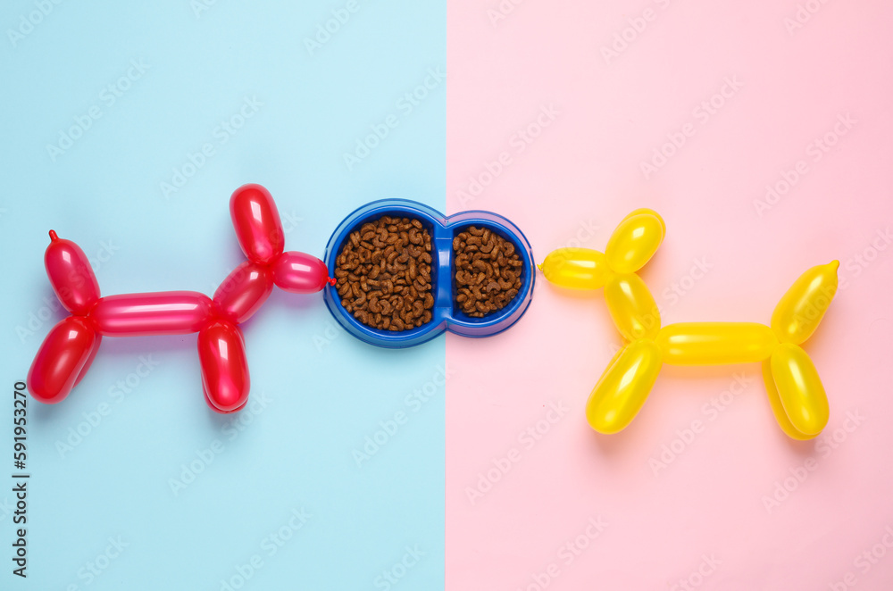 Balloon dogs and bowl of dog food on blue pink background. Top view