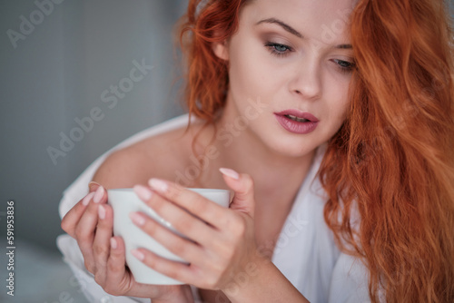 Fototapeta Naklejka Na Ścianę i Meble -  A young, red-haired woman in an apartment in the morning, Sunday rest with coffee