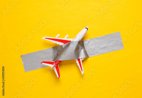 Toy airplane fixed with adhesive tape on yellow background. Conceptual pop, contemporary art, travel concept