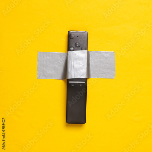 Fotografie Tv remote fixed with adhesive tape on yellow background