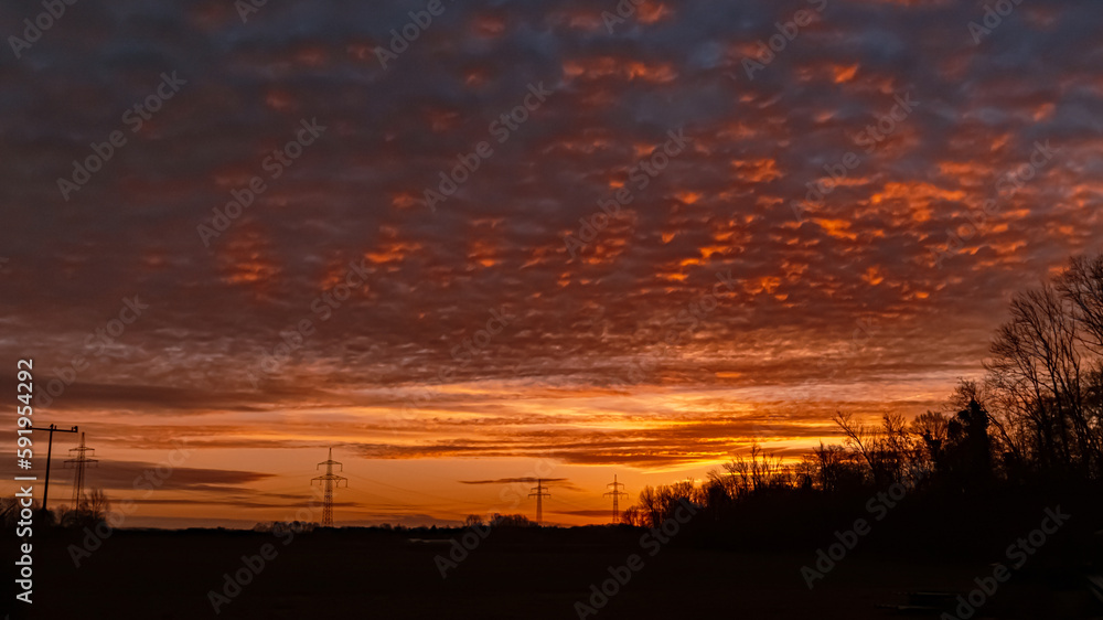 Winter sunrise with a dramatic sky and overland high voltage lines near Tabertshausen, Bavaria, Germany