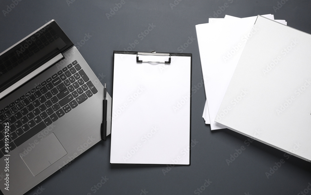 Laptop, Clipboard with white blank sheets of paper and a pen, folder on a dark background. Business concept. Top view, flat lay Laptop, Clipboard with white blank sheets of paper and a pen, folder on a dark background. Business concept. Top view, flat lay