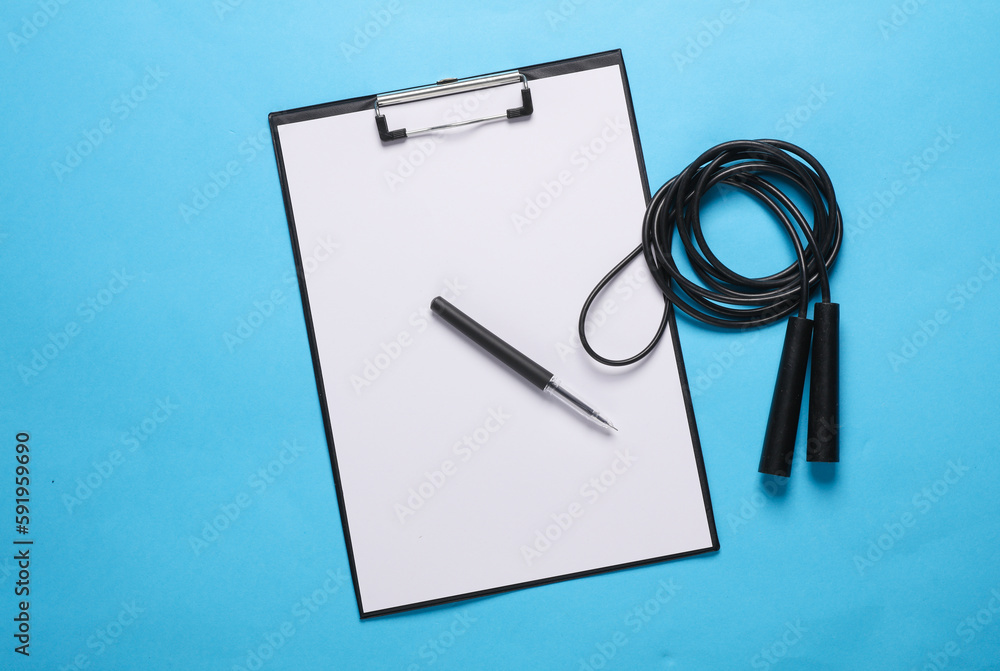 Workout plan, bodybuilding and fitness, weight loss. Clipboard with jump rope on blue background. Flat lay. Top view Workout plan, bodybuilding and fitness, weight loss. Clipboard with jump rope on blue background. Flat lay. Top view