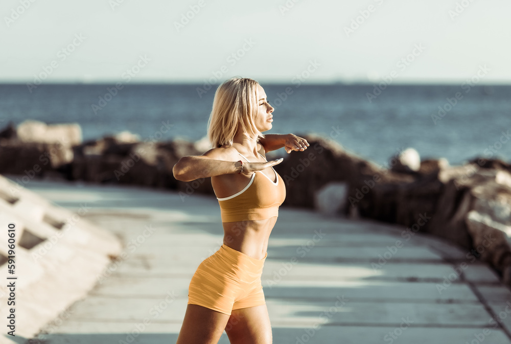 Young athletic muscular blonde woman practicing warm-up exercising outdoors on bright sunny day