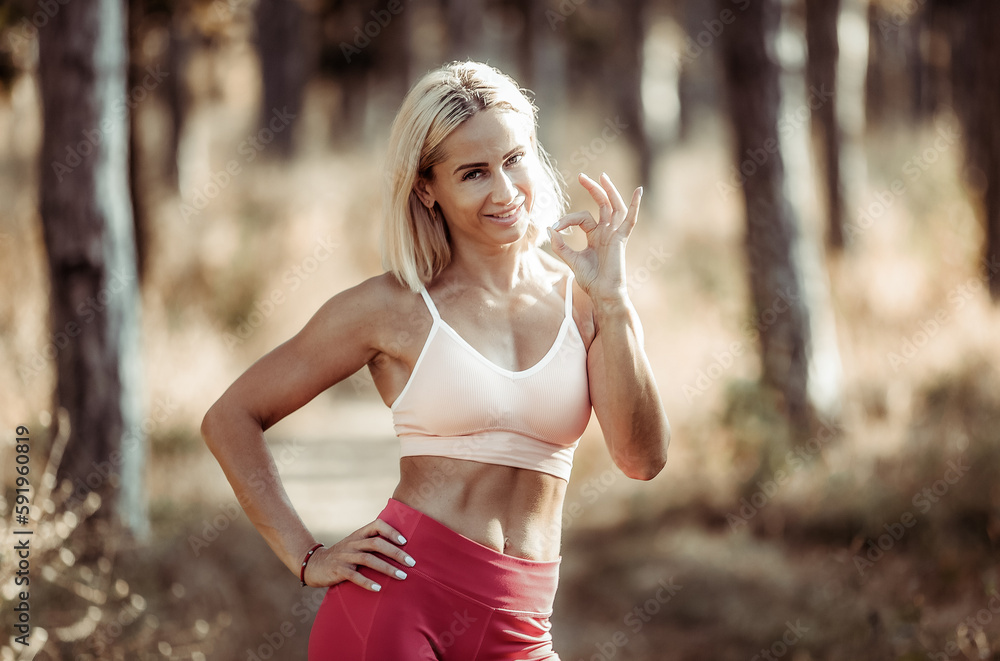 Young smiling fit woman in sports clothes shows okay gesture in the forest Young smiling fit woman in sports clothes shows okay gesture in the forest