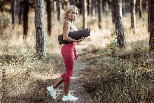 Portrait of athletic woman with rolled up yoga mat in forest