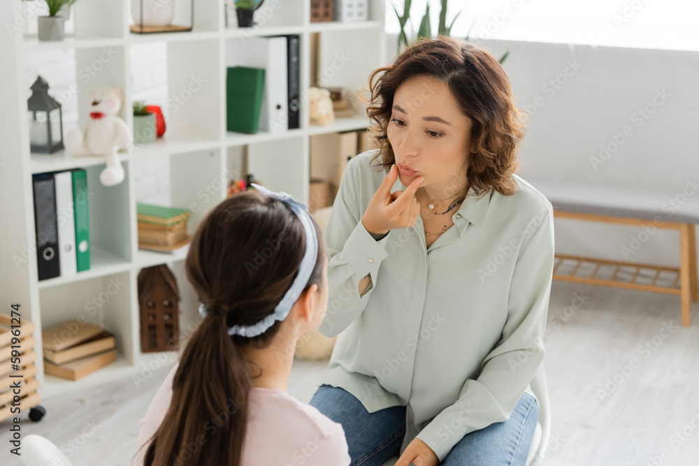 Speech therapist touching mouth during lesson with child in consulting room.