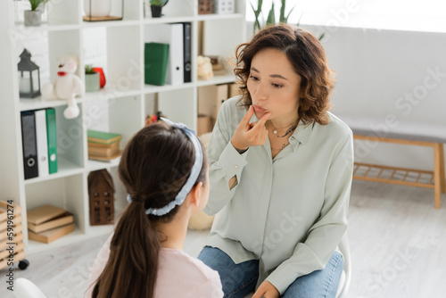 Speech therapist touching mouth during lesson with child in consulting room.
