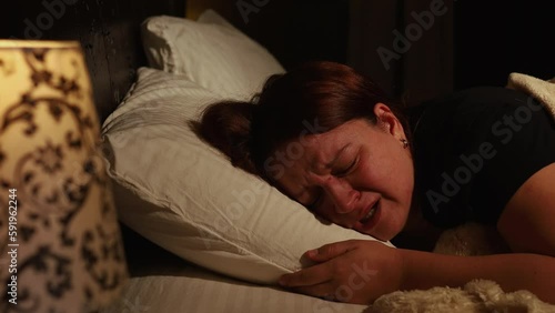 Distressed woman lie on pillow in bed and cry bitterly in dark bedroom. Splash out emotions, sob with tears. Emotional breakdown, stress, sufferings. Depression, night hysterics before sleep. photo