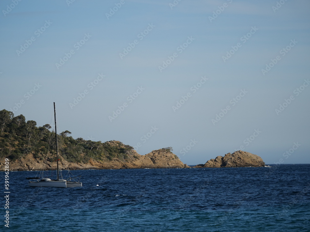 Ein Segelboot auf dem Meer, im Hintergrund sind Felsen einer Insel Ein Segelboot auf dem Meer, im Hintergrund sind Felsen einer Insel