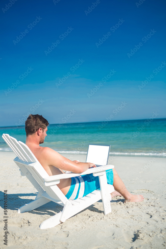 Man using laptop on deck chair at the beach