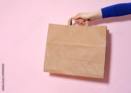 Female hand holding a paper bag with delivered items. Pink background